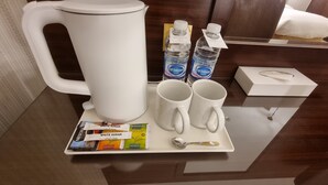 Une chambre d’hôtel équipée d’une machine à café, de deux bouteilles d’eau, d’un plateau avec des sachets de thé et d’une cuillère.