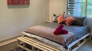 A bedroom with a bed, a standing desk, a window with a view, and a ceiling fan. - Perfect little home away from home in the tropics. (Parap)