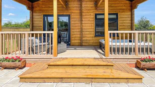 A wooden cabin with a covered porch, a hot tub, and a seating area with cushions. - Indulge and delight at this wonderful lodge, with your own private hot tub. (Halstead)