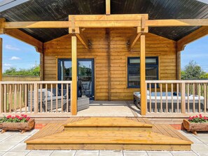 A wooden cabin with a covered porch, a hot tub, and a seating area with cushions. - Indulge and delight at this wonderful lodge, with your own private hot tub. (Halstead)