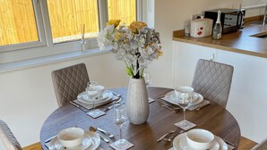 A round dining table set for four with white plates, silverware, and a vase of flowers. - Indulge and delight at this wonderful lodge, with your own private hot tub. (Halstead)