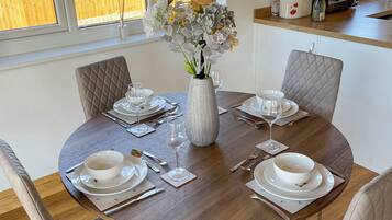 A round dining table set for four with white plates, silverware, and a vase of flowers.