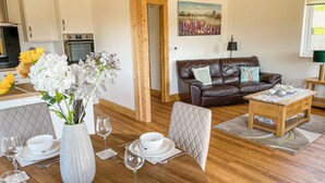 A modern living room with a dining area, wooden flooring, a brown leather sofa, and a painting on the wall. - Indulge and delight at this wonderful lodge, with your own private hot tub. (Halstead)