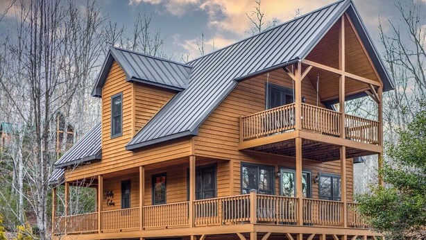 Een houten vakantiehuis met twee verdiepingen en een balkon op de bovenverdieping, omringd door bomen.
