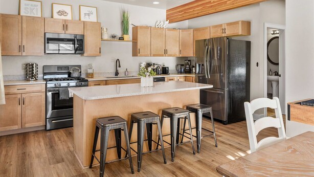 A modern kitchen with wooden cabinets, stainless steel appliances, a central island with stools, and a wooden ceiling. - Modern Red Lodge Cabin - Walk to Broadway Ave (Red Lodge)