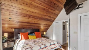 A bedroom with a sloped ceiling, a bed with patterned bedding, and a nightstand with a lamp. - Modern Red Lodge Cabin - Walk to Broadway Ave (Red Lodge)