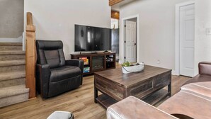 A living room with a TV, leather sofa, coffee table, and a staircase. - Modern Red Lodge Cabin - Walk to Broadway Ave (Red Lodge)