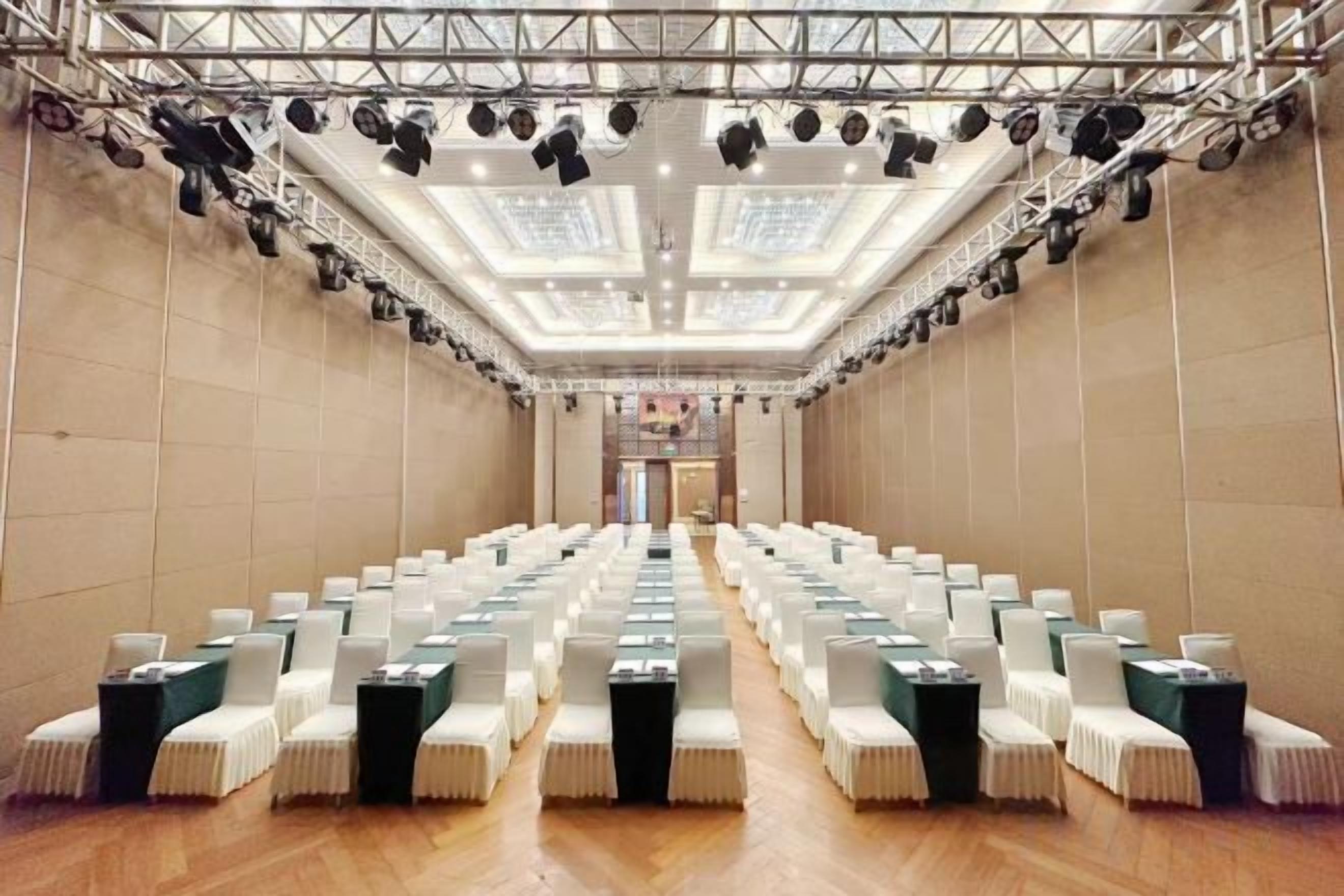 A conference room with rows of chairs, a stage with lighting, and a high ceiling.