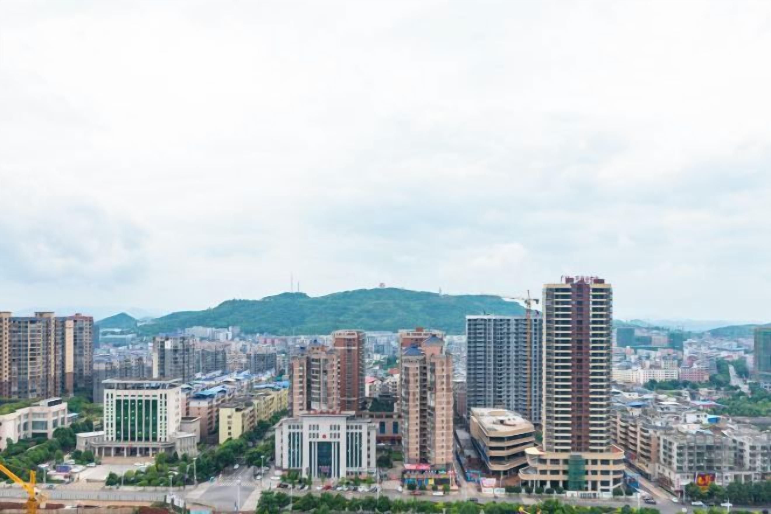 Un paisaje urbano con edificios altos, una grúa de construcción y un fondo montañoso.