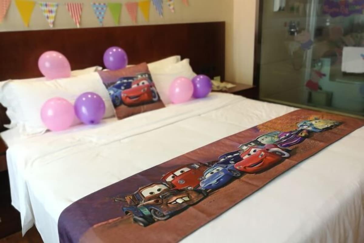 Una cama con edredón de motivos de coches, almohadas y globos.