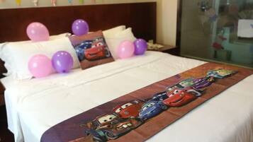 Una cama con edredón de motivos de coches, almohadas y globos.