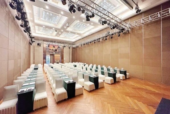 A conference room with rows of chairs, a stage with lighting, and a wooden floor.
