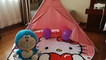 Uma estrutura tipo tenda com design de Hello Kitty, um brinquedo de pelúcia azul e balões roxos no chão.