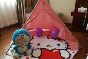 Una estructura tipo tienda con diseño de Hello Kitty, un peluche azul y globos morados sobre un suelo.