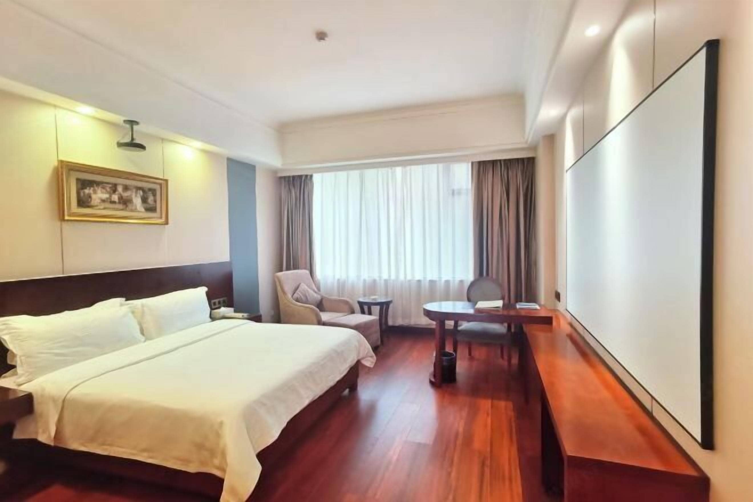 A hotel room with a bed, a chair, a small table, and a large window with curtains.