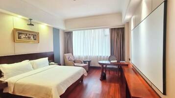 A hotel room with a bed, a chair, a small table, and a large window with curtains.
