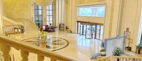 A grand lobby with a central staircase, a chandelier, and a large window.