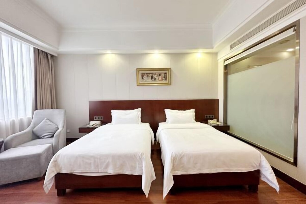 Habitación de hotel con dos camas individuales, una silla, una mesita de noche y un ventanal grande.