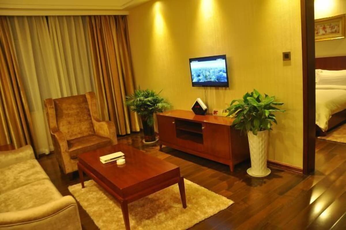 Una habitación de hotel con una mesa de centro de madera, un sofá, un televisor montado en la pared y una cama.