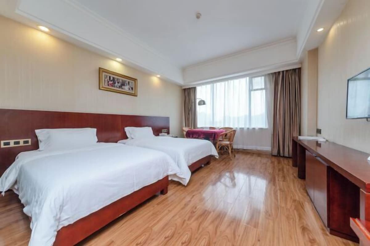 Habitación de hotel con dos camas, un escritorio, una silla, un televisor y una ventana con cortinas.