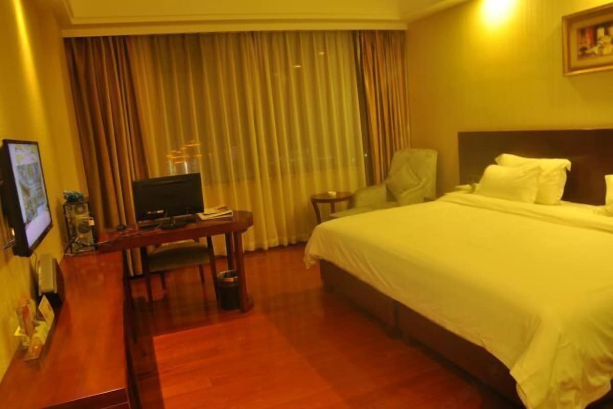 Una habitación de hotel con una cama, un escritorio con televisión, una silla y un ventanal con cortinas.