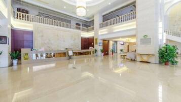 A spacious lobby with a marble reception desk, multiple floors, and a central atrium with a glass ceiling.