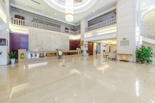 Un vestíbulo espacioso con una recepción de mármol, varios pisos y un atrium central con techo de cristal.