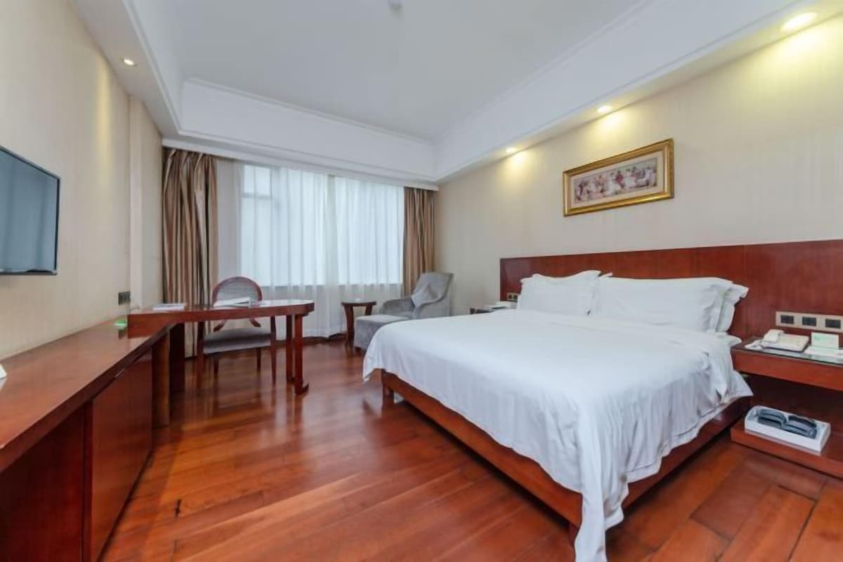 Habitación de hotel con una cama grande, un escritorio, una silla, un televisor y una ventana con cortinas.