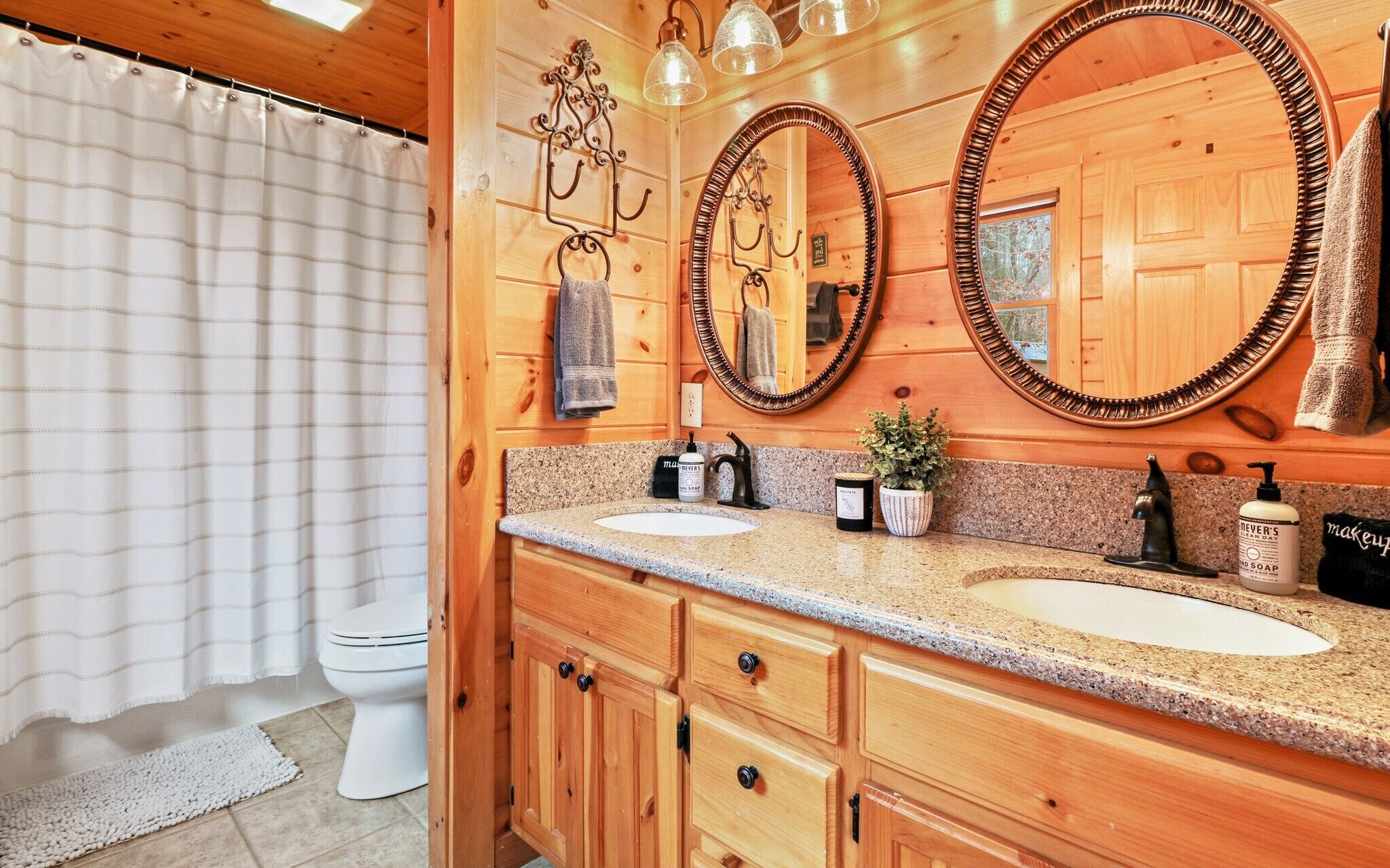 A wooden bathroom with two sinks, a toilet, and a shower curtain.