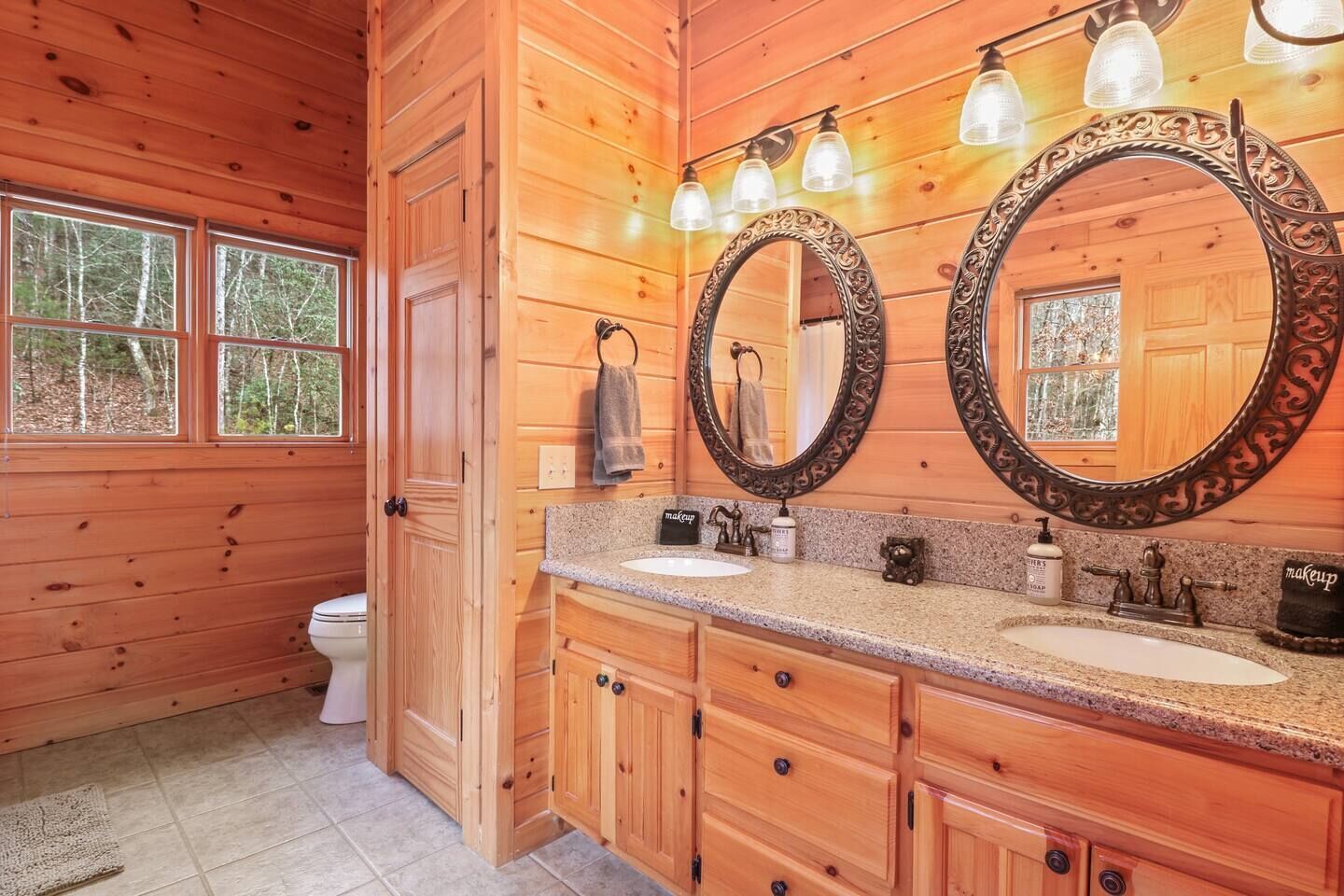 A wooden cabin bathroom with two sinks, a toilet, and large mirrors.