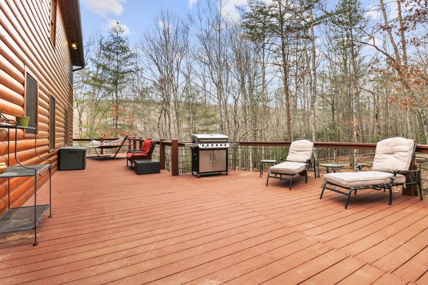 A wooden deck with outdoor furniture, a grill, and a view of a forest.