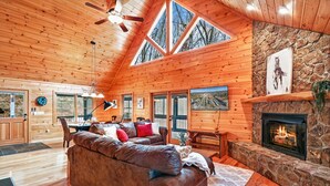 Een gezellig chaletinterieur met een stenen openhaard, houten plafond en grote ramen.