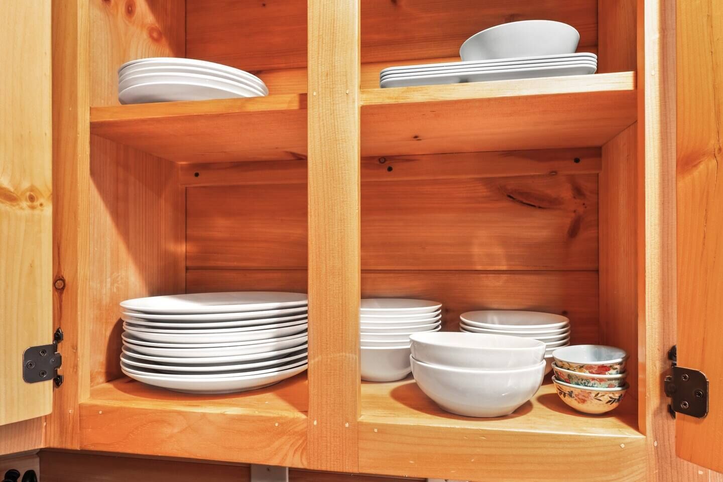 A wooden cabinet with multiple shelves holding white plates and bowls.