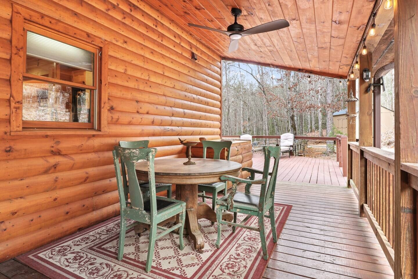 Eine Holzhütte mit rundem Tisch und Stühlen auf einer Veranda, umgeben von einem Wald.