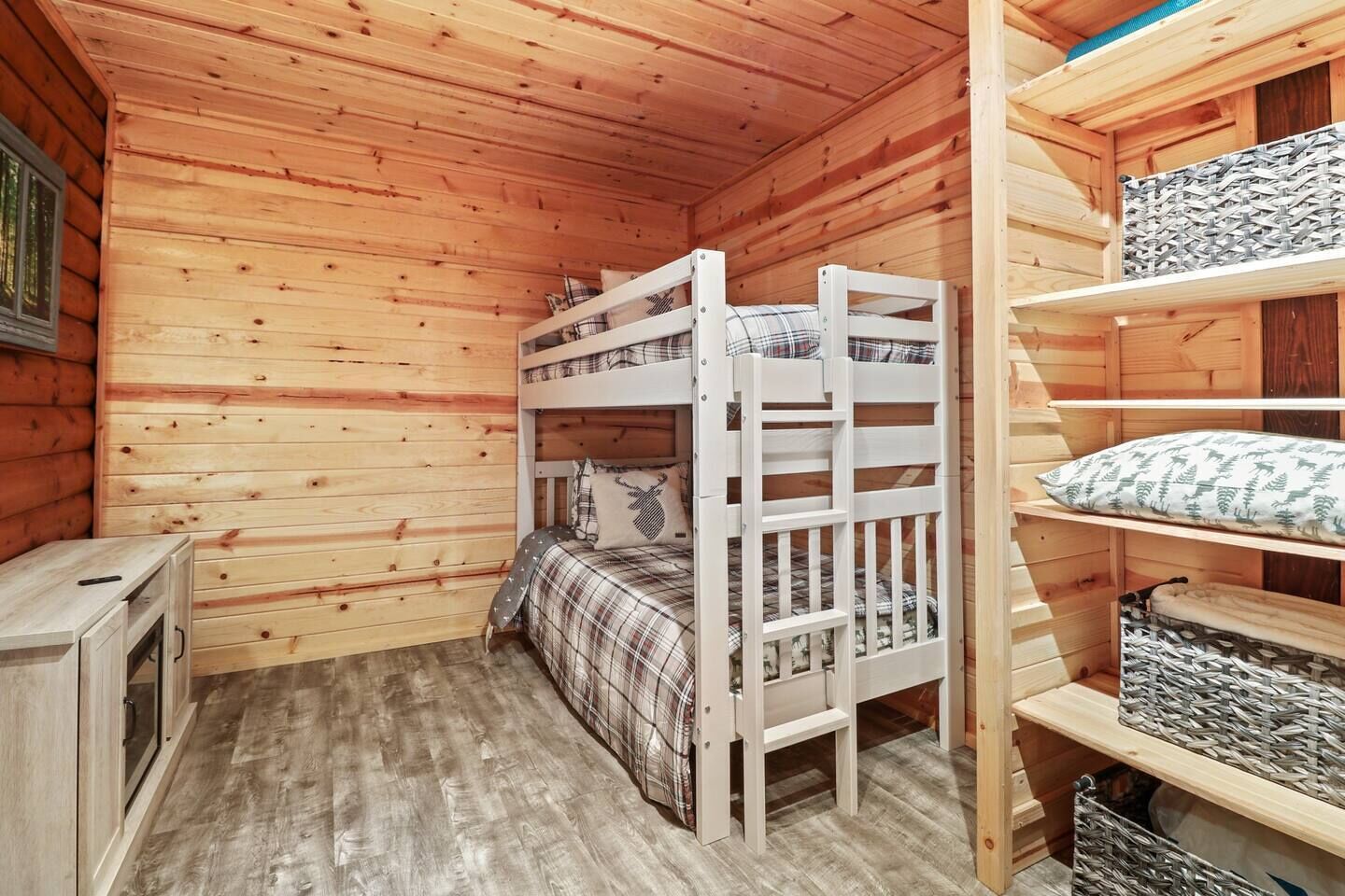 A wooden cabin room with bunk beds, a small cabinet, and shelves with storage baskets.