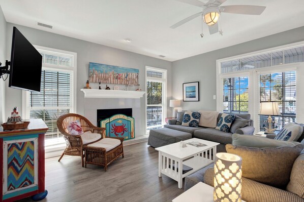 A spacious living room with a fireplace, comfortable seating, and large windows offering a view of the outdoors.