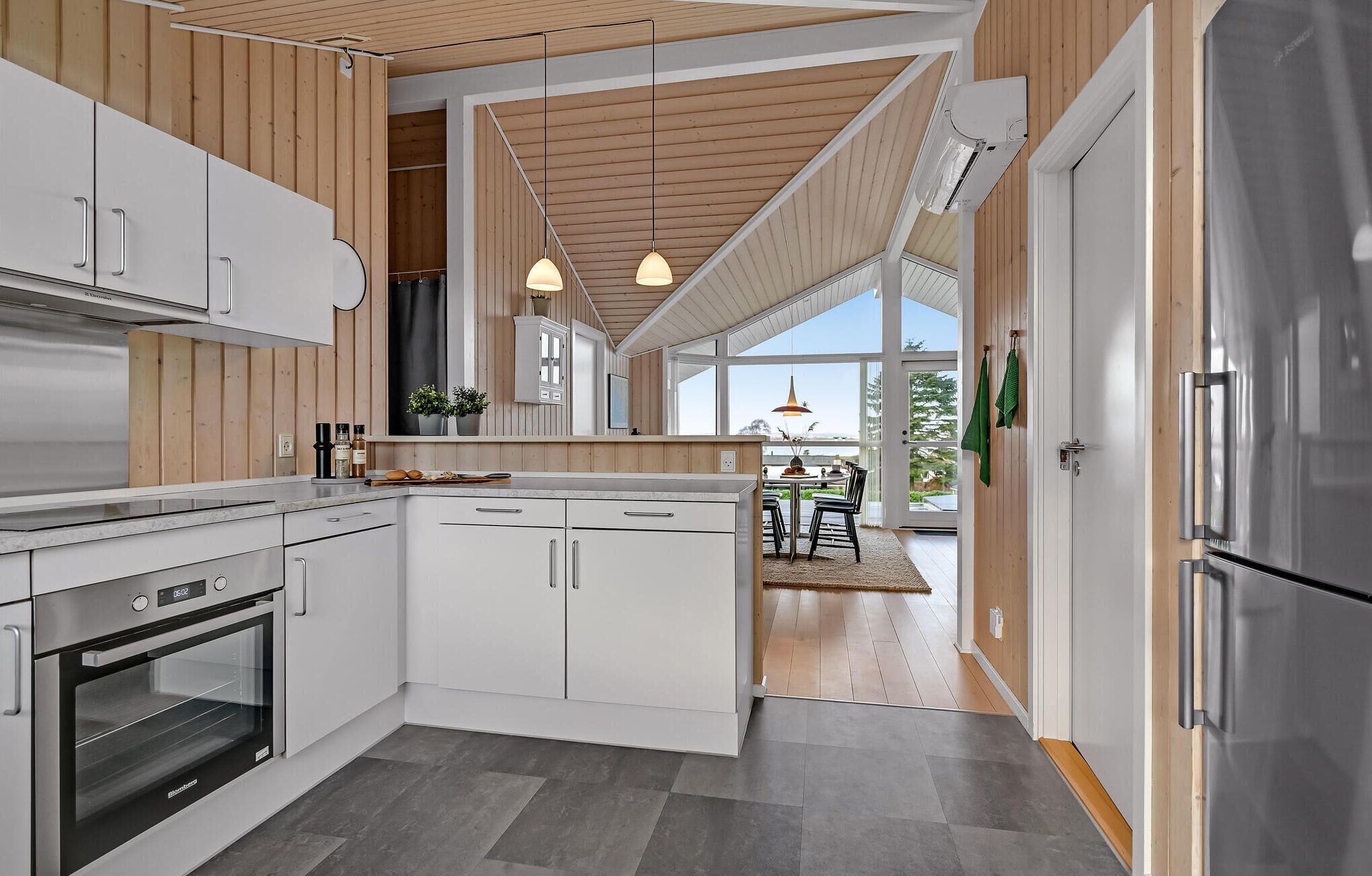 Une cuisine moderne avec des meubles blancs, un four encastré et des luminaires suspendus.