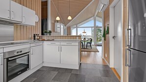 Moderni keittiö, jossa on valkoiset kaapit, sisäänrakennettu uuni ja riippuvalaisimet.