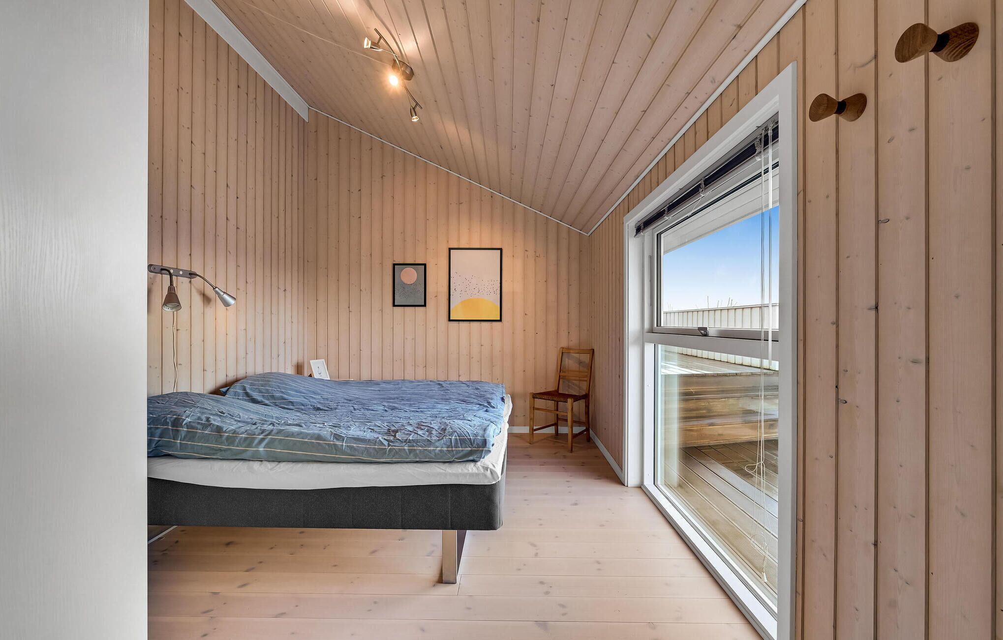Um quarto com uma cama, uma cadeira, uma janela e paredes de madeira.