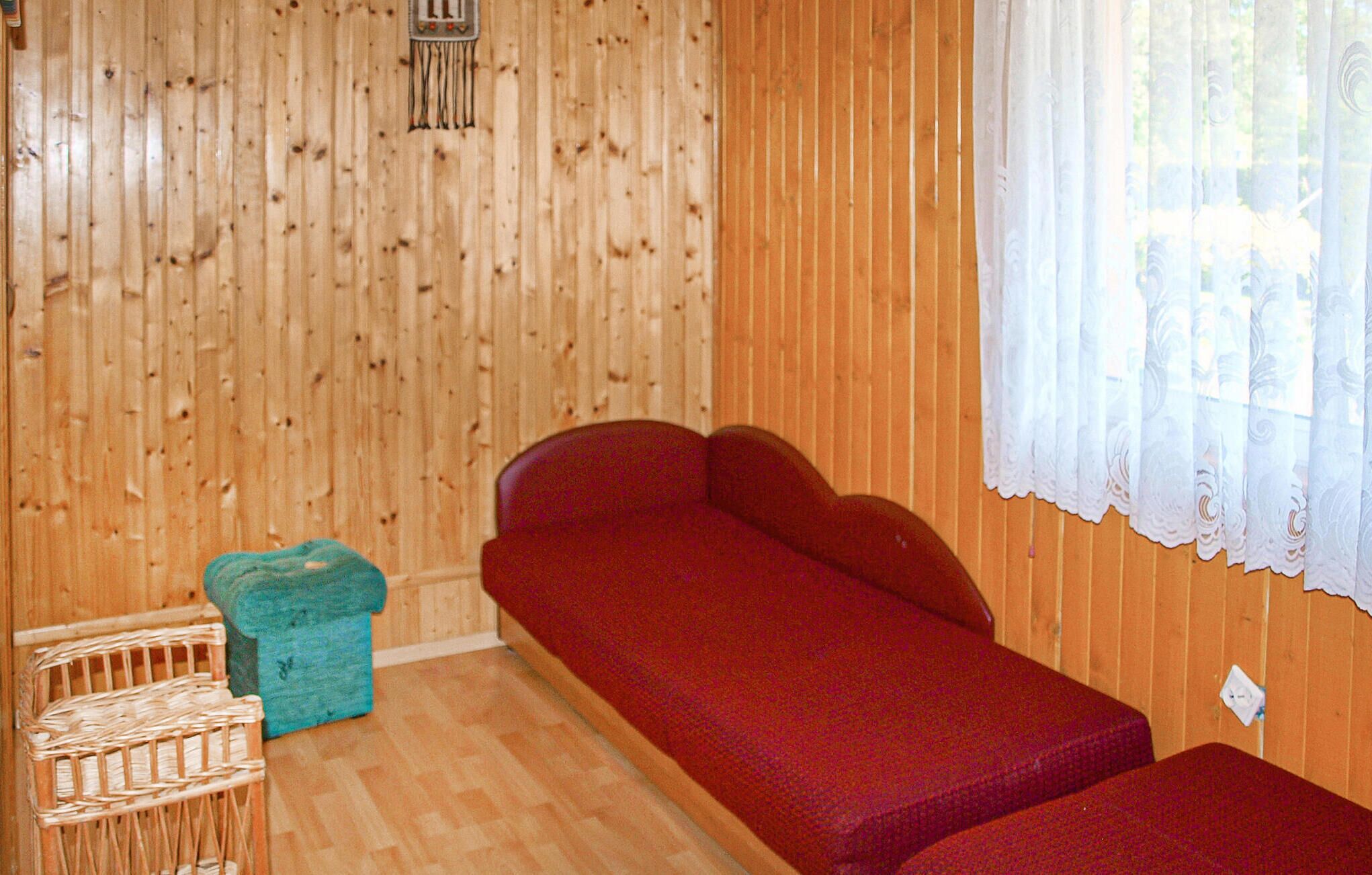 Una habitación con paredes de madera, un sofá rojo, una silla pequeña azul y una silla de mimbre.