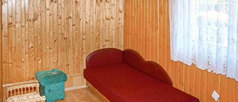 Una habitación con paredes de madera, un sofá rojo, una silla pequeña azul y una silla de mimbre.