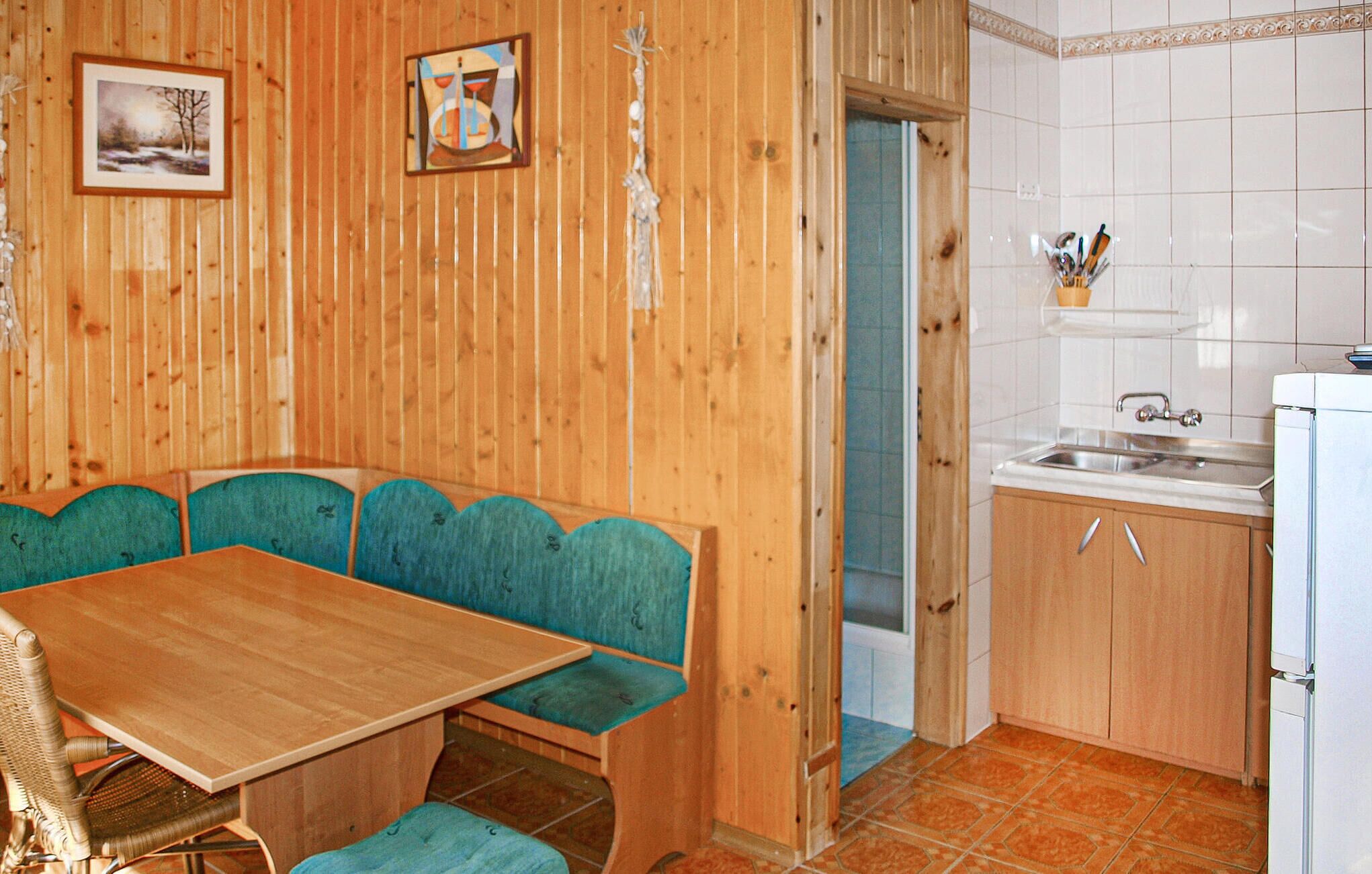 A wooden interior with a dining table and benches, a kitchen area with a sink and cabinets, and two framed pictures on the wall.