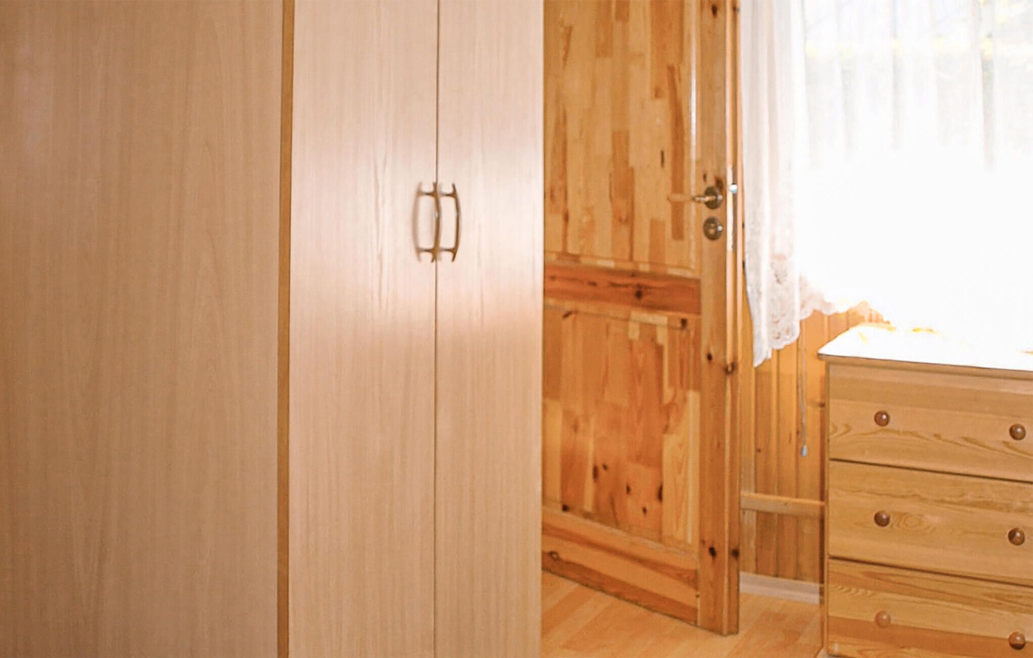 A wooden wardrobe with a mirror, a wooden dresser with drawers, and a partially open door revealing a wooden closet.