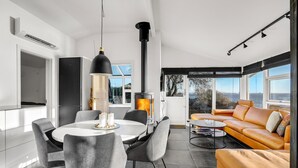 A modern living room with a round dining table, grey chairs, a sofa, and a large window offering a view of the sea. - 2 bedroom amazing home in Otterup (Otterup)