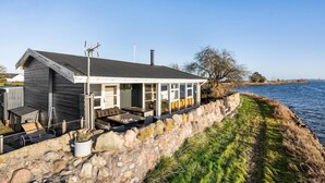 A coastal house with a stone wall, a covered patio, and a view of the sea. - 2 bedroom amazing home in Otterup (Otterup)