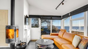 A modern living room with a large window, a sofa, a fireplace, and a coffee table. - 2 bedroom amazing home in Otterup (Otterup)