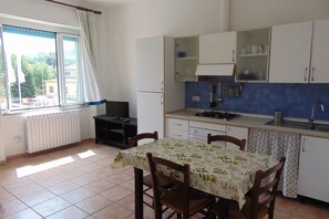 Une cuisine équipée d’une table à manger, de chaises, de placards, d’une fenêtre avec des rideaux et d’un radiateur.