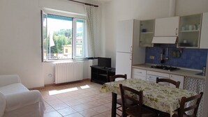 Una pequeña cocina con una mesa, sillas, un sofá blanco y un ventanal con cortinas.