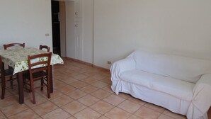 Una habitación con una mesa de comedor, sillas, un sofá blanco y piso de baldosas.