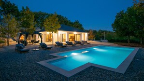 Ett modernt hus med en swimmingpool, utomhusmöbler och en väl upplyst uteplats.